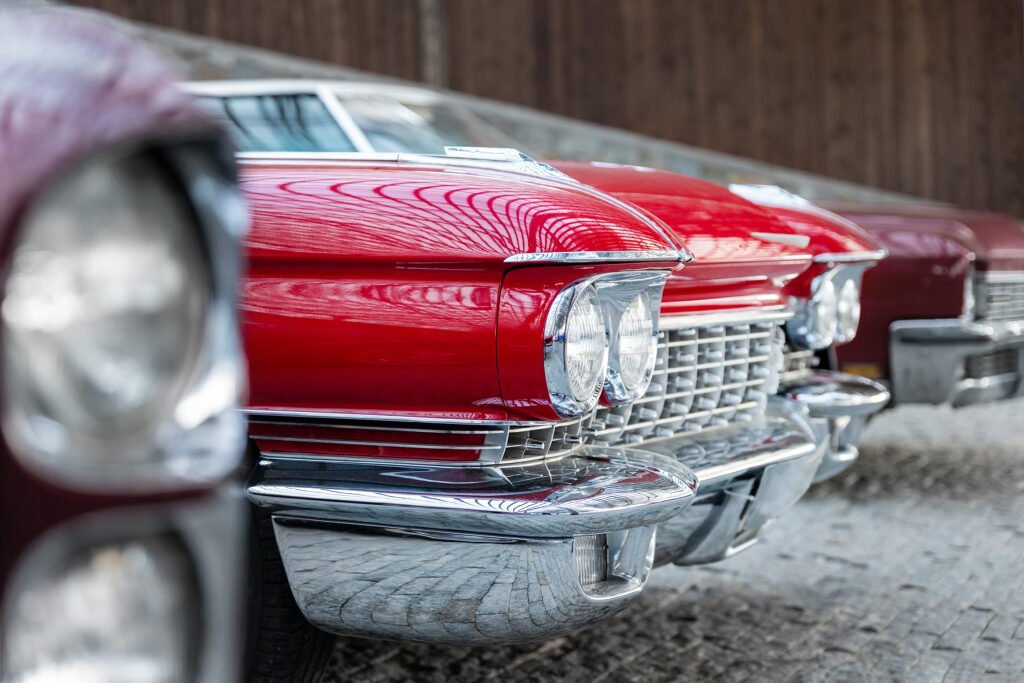 many classic red vintage old american cars parked in row at garage, exhibition of fest. close up detail view beautiful retro oldtimer vehicle hood, headlight, fender and shine chrome plated bumper